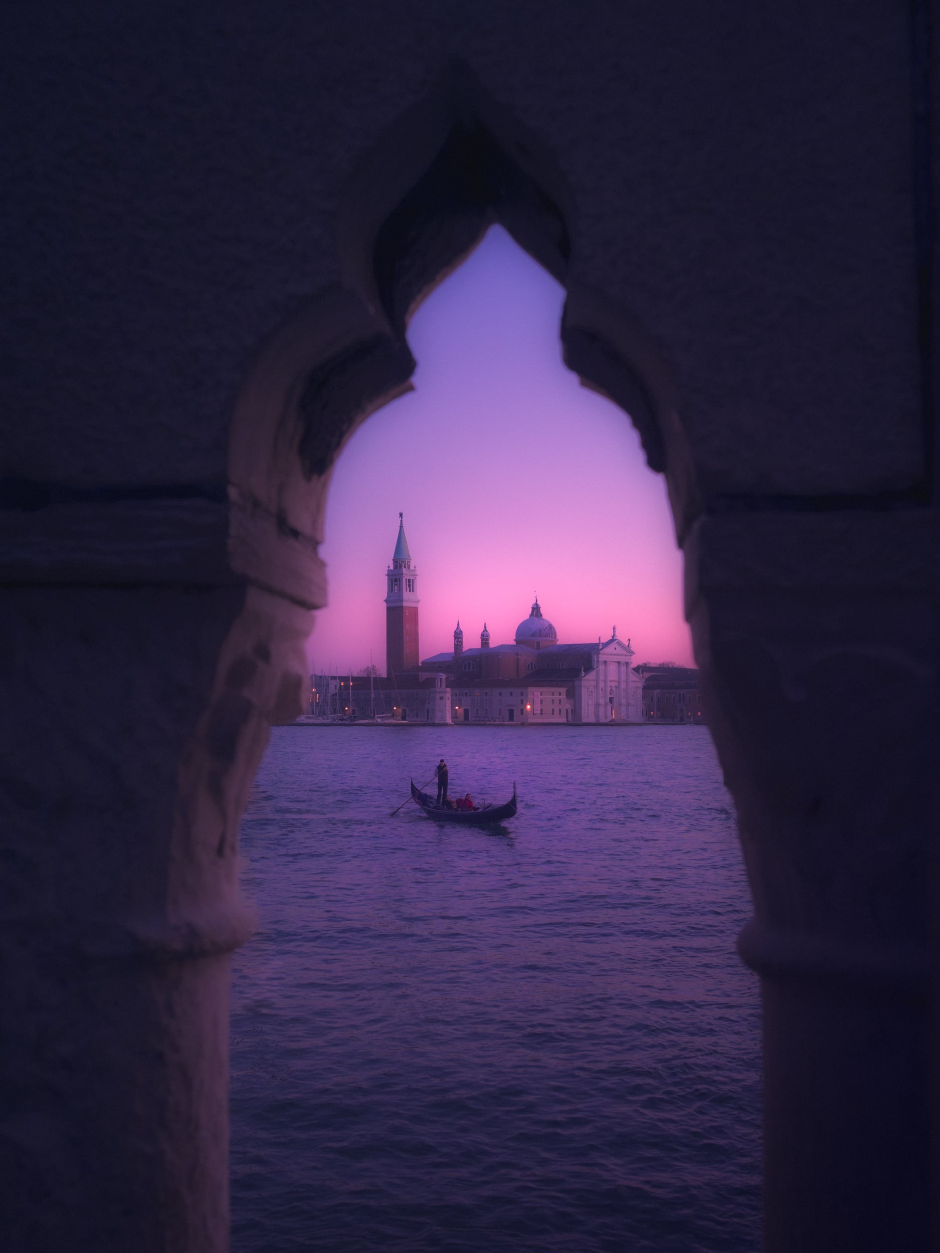 San Giorgio Maggiore al atardecer, enmarcada por un arco gótico, con una góndola cruzando la laguna de Venecia.